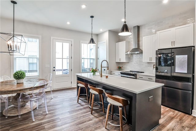 kitchen featuring an island with sink, wall chimney range hood, appliances with stainless steel finishes, and wood finished floors