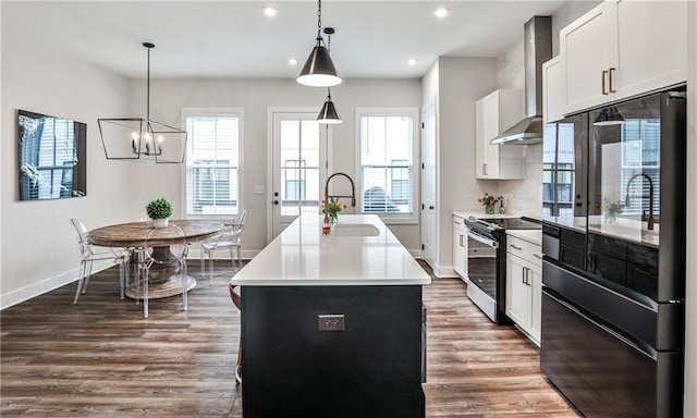 kitchen with electric stove, dark wood-style flooring, black fridge, wall chimney range hood, and a sink