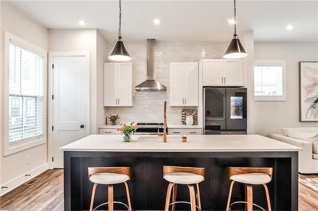 kitchen featuring a breakfast bar, wall chimney range hood, refrigerator with glass door, and decorative backsplash