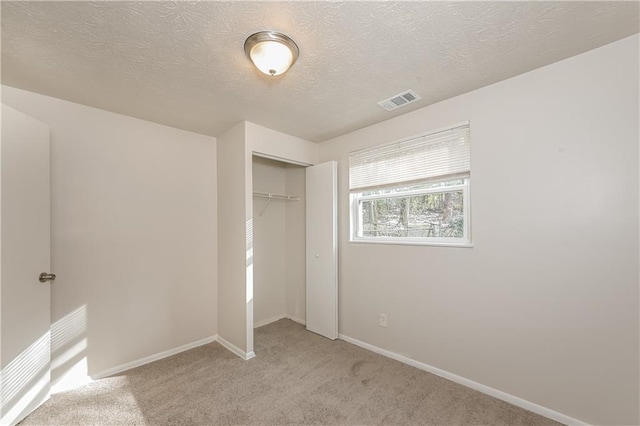 unfurnished bedroom with light colored carpet, a textured ceiling, and a closet