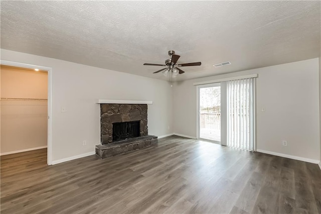 unfurnished living room with ceiling fan, a textured ceiling, dark hardwood / wood-style flooring, and a stone fireplace