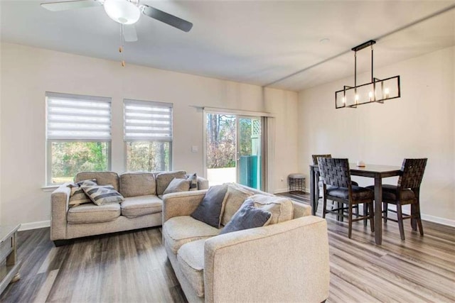 living room with ceiling fan with notable chandelier, a healthy amount of sunlight, baseboards, and wood finished floors