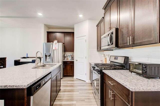 kitchen featuring a sink, light wood-style floors, dark brown cabinets, appliances with stainless steel finishes, and tasteful backsplash