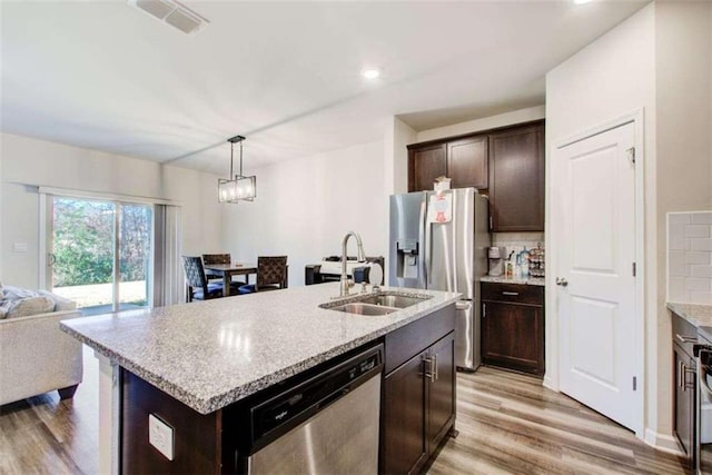 kitchen featuring light wood finished floors, decorative backsplash, appliances with stainless steel finishes, open floor plan, and dark brown cabinets