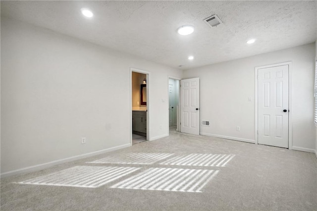 unfurnished bedroom with light carpet, a textured ceiling, and ensuite bathroom