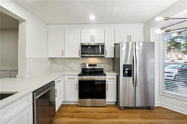 kitchen featuring light stone countertops, appliances with stainless steel finishes, tasteful backsplash, light hardwood / wood-style flooring, and white cabinets