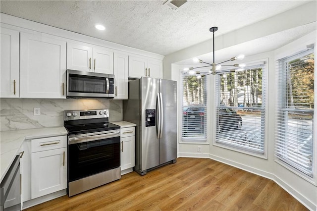 kitchen featuring white cabinetry, a notable chandelier, pendant lighting, light hardwood / wood-style floors, and appliances with stainless steel finishes