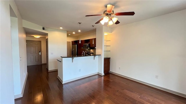 kitchen with kitchen peninsula, appliances with stainless steel finishes, a breakfast bar, and dark wood-type flooring