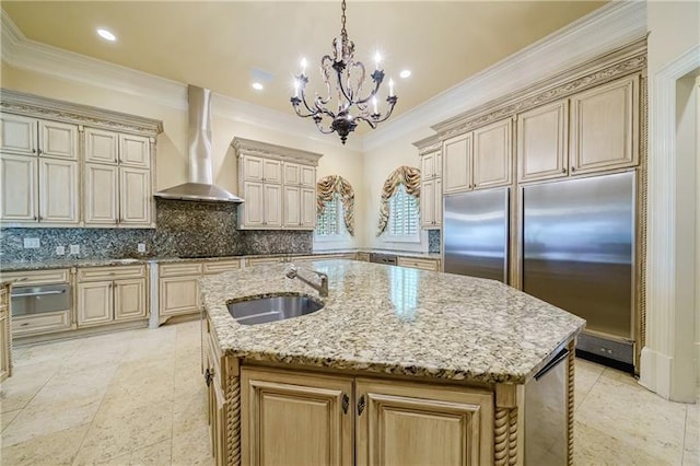 kitchen with pendant lighting, sink, an island with sink, wall chimney exhaust hood, and light stone counters