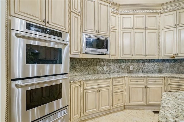 kitchen featuring cream cabinetry, decorative backsplash, light stone counters, and stainless steel appliances