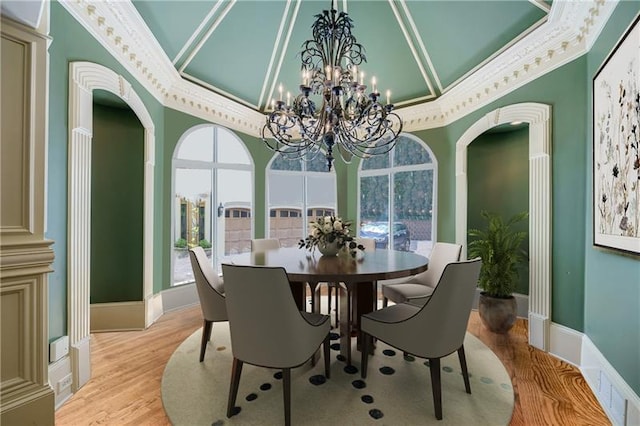 dining room featuring wood-type flooring, crown molding, a towering ceiling, and an inviting chandelier