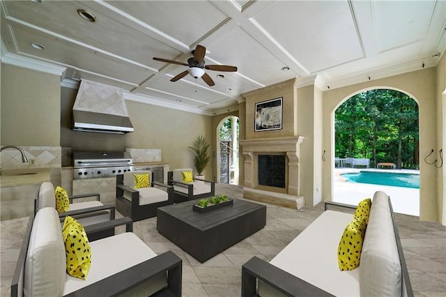 living room featuring exterior fireplace, ceiling fan, coffered ceiling, and sink