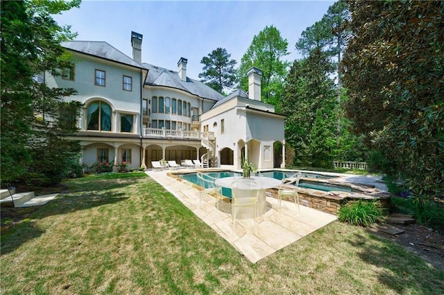 rear view of property with a balcony, a yard, a swimming pool with hot tub, and a patio