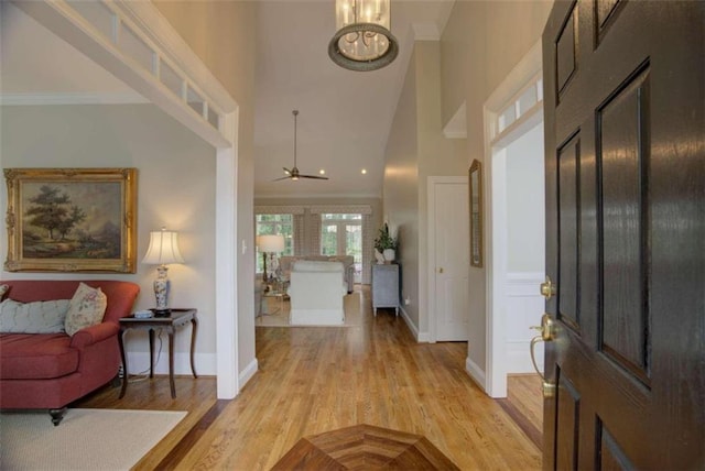 foyer with light hardwood / wood-style flooring, ornamental molding, a high ceiling, and ceiling fan