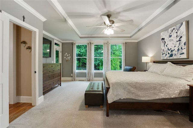 bedroom with a tray ceiling, ornamental molding, carpet floors, baseboards, and ceiling fan