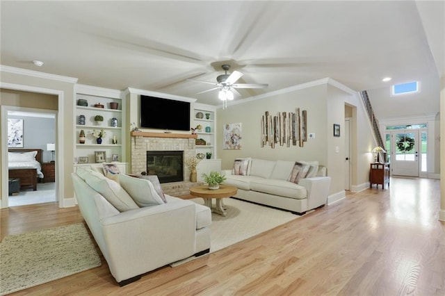 living area featuring a fireplace, ceiling fan, wood finished floors, baseboards, and crown molding