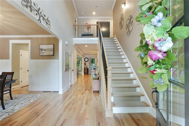 foyer featuring ornamental molding, wood finished floors, stairway, a wainscoted wall, and a towering ceiling