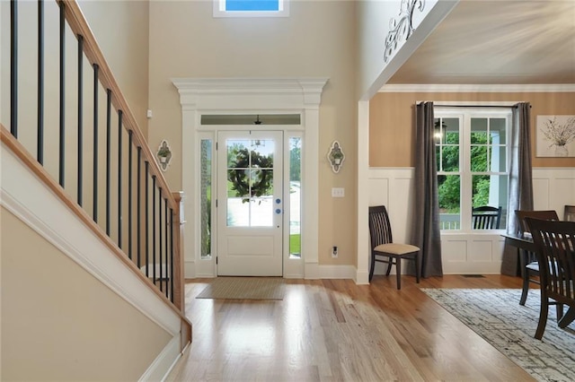 entrance foyer with healthy amount of natural light, stairs, wood finished floors, a towering ceiling, and a wainscoted wall