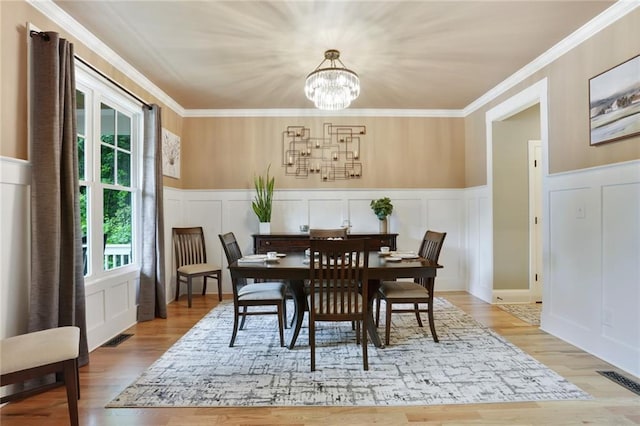 dining space with a decorative wall, a chandelier, wood finished floors, ornamental molding, and a wainscoted wall