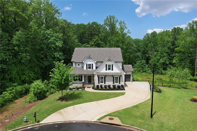 view of front of house with driveway, a front lawn, a garage, and a wooded view