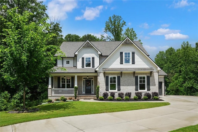 craftsman inspired home featuring covered porch, a front lawn, brick siding, concrete driveway, and a shingled roof