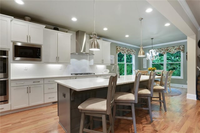 kitchen featuring wall chimney range hood, stainless steel microwave, a sink, light countertops, and decorative backsplash