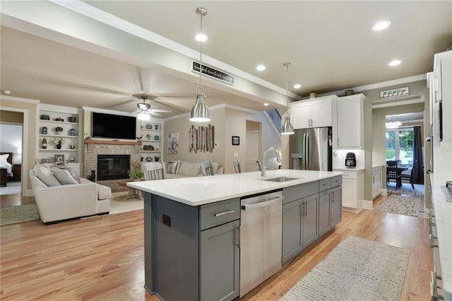 kitchen featuring gray cabinetry, a sink, appliances with stainless steel finishes, a ceiling fan, and a center island with sink
