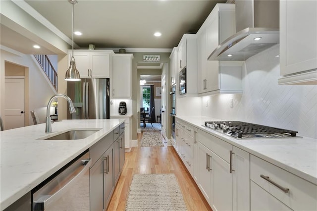 kitchen featuring a sink, wall chimney exhaust hood, stainless steel appliances, crown molding, and hanging light fixtures