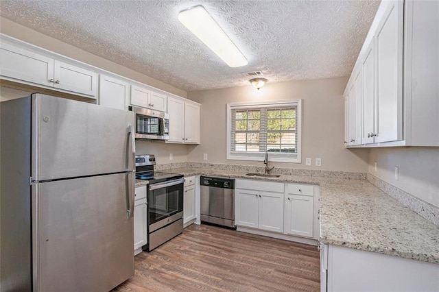 kitchen featuring white cabinets, appliances with stainless steel finishes, wood finished floors, light stone countertops, and a sink