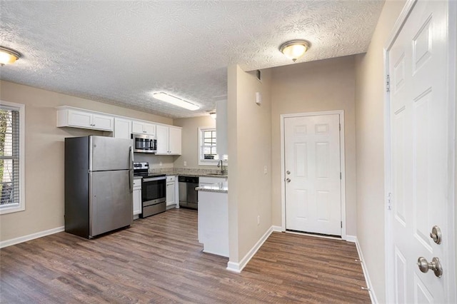 kitchen with stainless steel appliances, dark wood-type flooring, white cabinetry, and baseboards