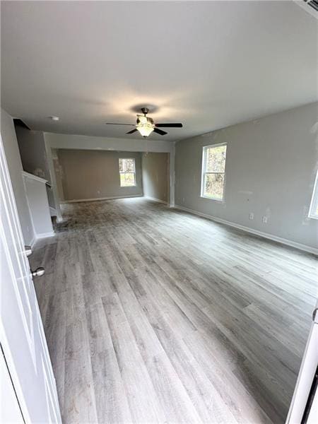 unfurnished living room with baseboards, plenty of natural light, wood finished floors, and a ceiling fan