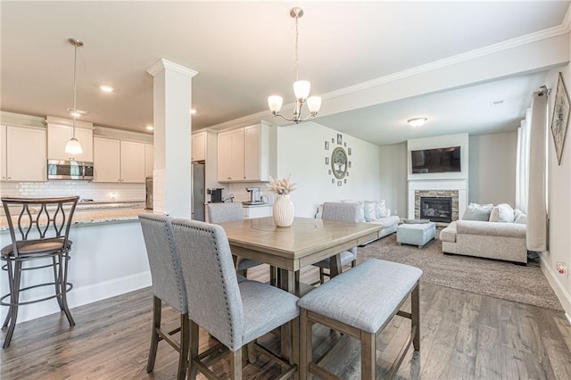 dining area featuring dark hardwood / wood-style flooring, crown molding, an inviting chandelier, and a fireplace