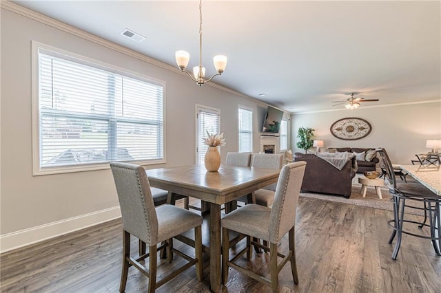 dining room with ornamental molding, ceiling fan with notable chandelier, and dark hardwood / wood-style flooring