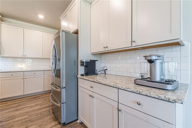 kitchen featuring stainless steel fridge, light stone counters, white cabinets, backsplash, and light wood-type flooring