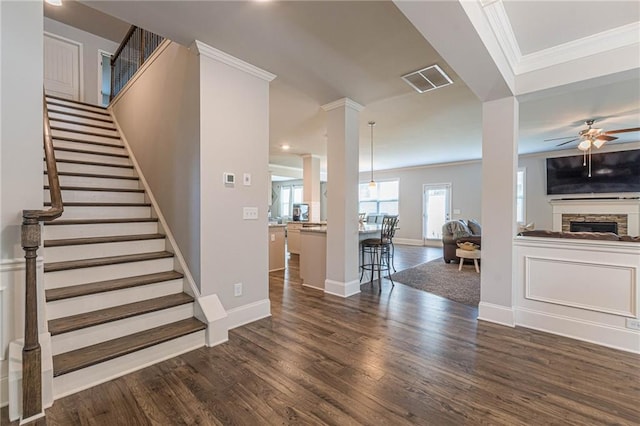 interior space featuring ornamental molding, a fireplace, ceiling fan, and dark wood-type flooring