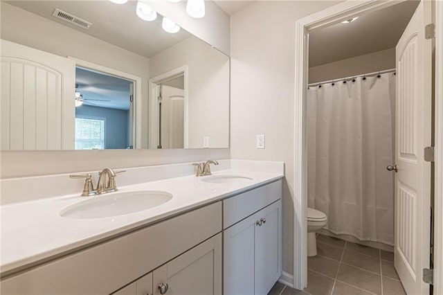 bathroom with double sink, oversized vanity, tile flooring, toilet, and ceiling fan