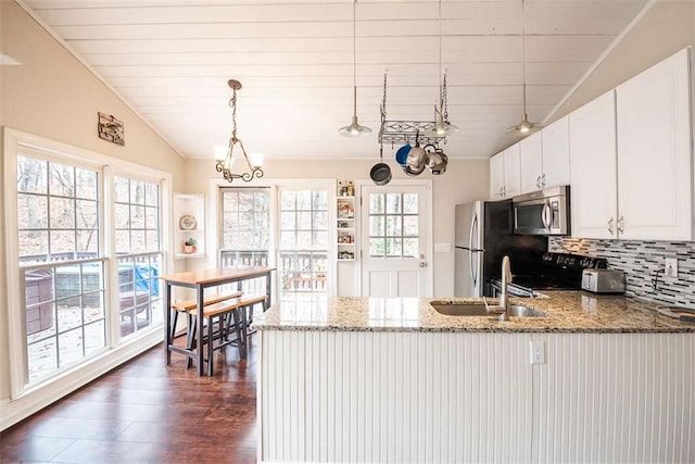 kitchen with lofted ceiling, appliances with stainless steel finishes, light stone countertops, and white cabinets