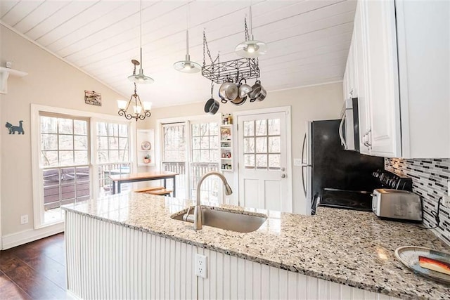 kitchen featuring stainless steel microwave, light stone countertops, white cabinetry, pendant lighting, and a sink