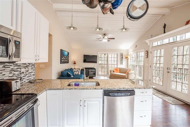 kitchen with light stone counters, decorative light fixtures, appliances with stainless steel finishes, white cabinets, and a sink