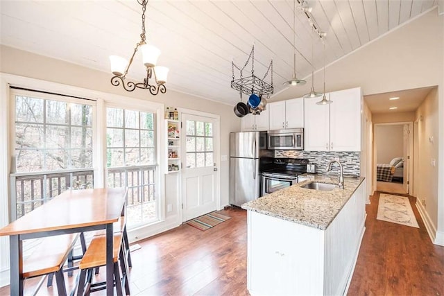 kitchen featuring pendant lighting, stainless steel appliances, white cabinetry, a sink, and light stone countertops