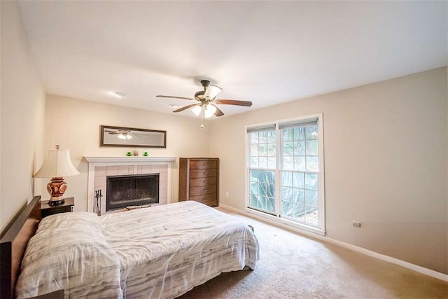 bedroom featuring carpet floors, ceiling fan, baseboards, and a tiled fireplace