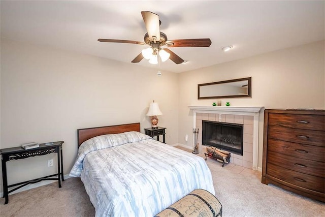 bedroom with ceiling fan, baseboards, a tiled fireplace, and light colored carpet