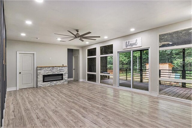 unfurnished living room featuring ceiling fan, a stone fireplace, light hardwood / wood-style flooring, and a wealth of natural light