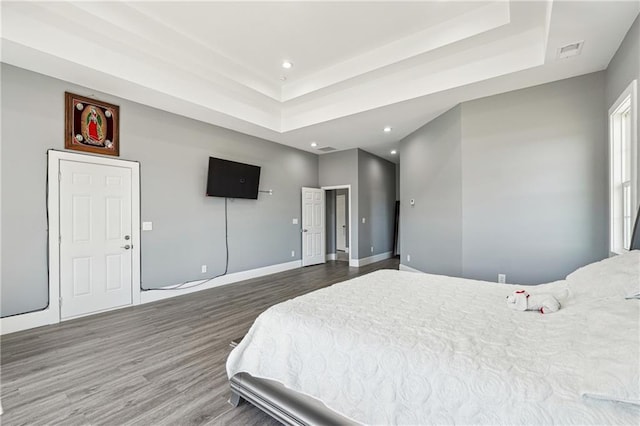 bedroom featuring visible vents, a raised ceiling, baseboards, and wood finished floors