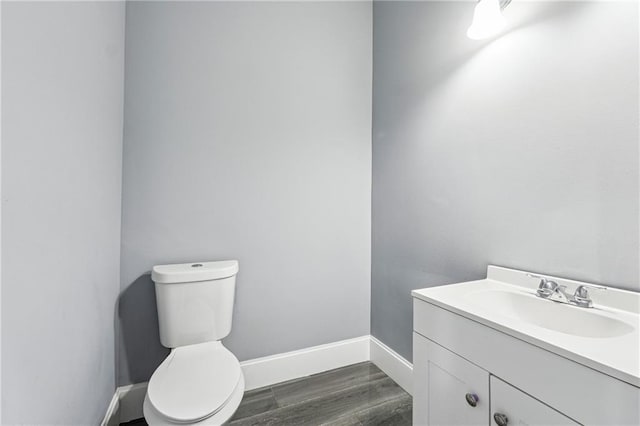 half bath featuring baseboards, toilet, wood finished floors, and vanity