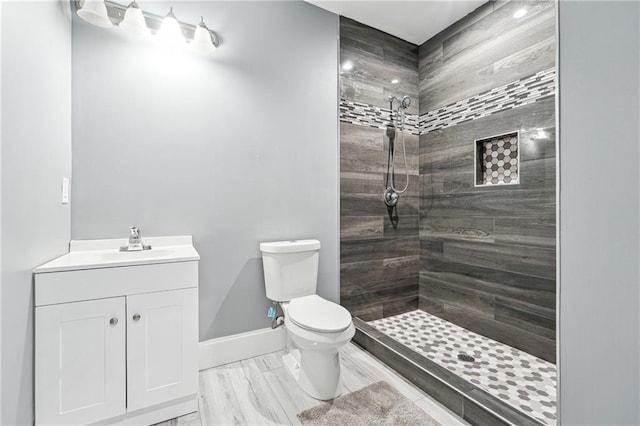 full bath with vanity, toilet, baseboards, and a tile shower