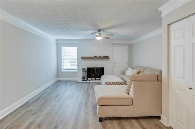 living room with ceiling fan, ornamental molding, light hardwood / wood-style floors, a textured ceiling, and a tiled fireplace