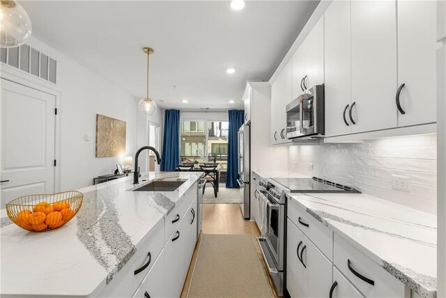 kitchen with white cabinetry, sink, pendant lighting, a center island with sink, and appliances with stainless steel finishes