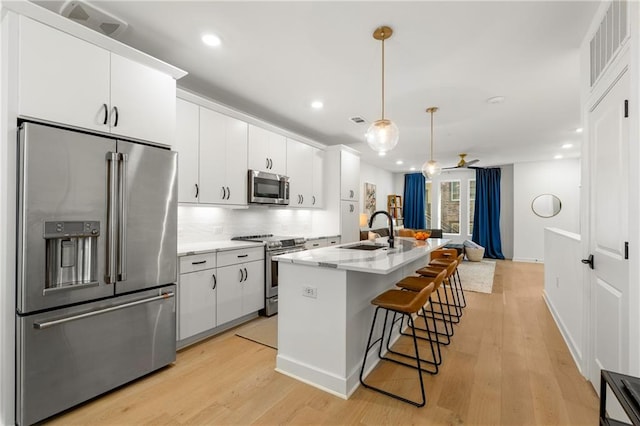 kitchen featuring light hardwood / wood-style floors, decorative light fixtures, a center island with sink, white cabinets, and appliances with stainless steel finishes