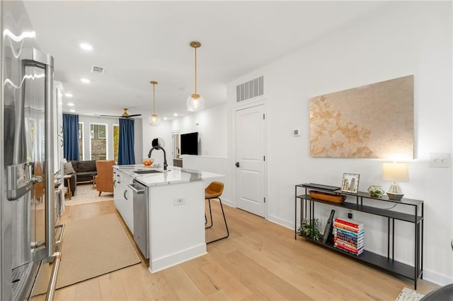 kitchen with hanging light fixtures, an island with sink, light wood-type flooring, white cabinets, and appliances with stainless steel finishes